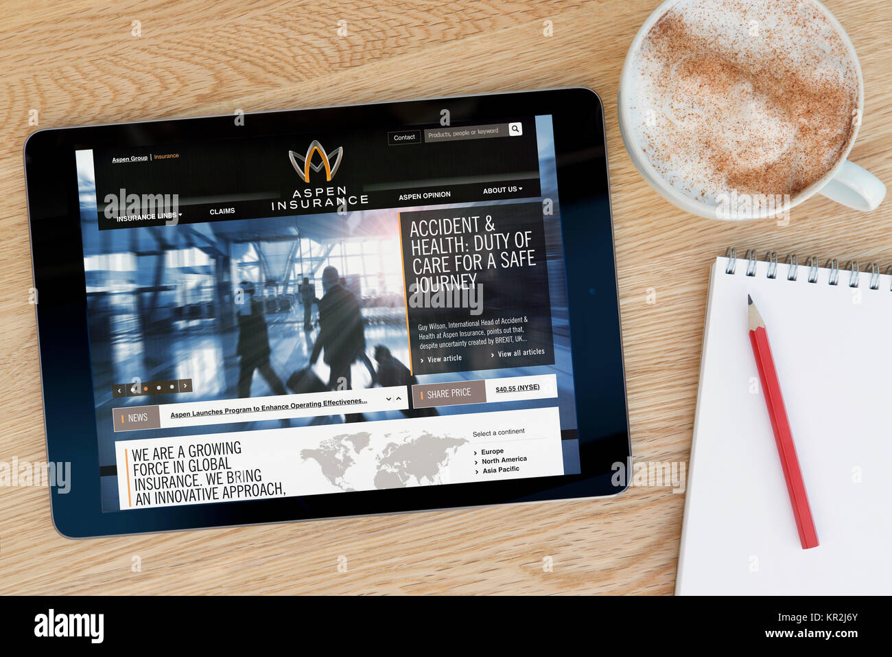 The Aspen Insurance website on an iPad tablet device which rests on a wooden table beside a notepad and pencil and a cup of coffee (Editorial only) Stock Photo