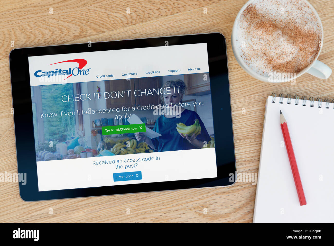 The Capital One website on an iPad tablet device which rests on a wooden table beside a notepad and pencil and a cup of coffee (Editorial only) Stock Photo