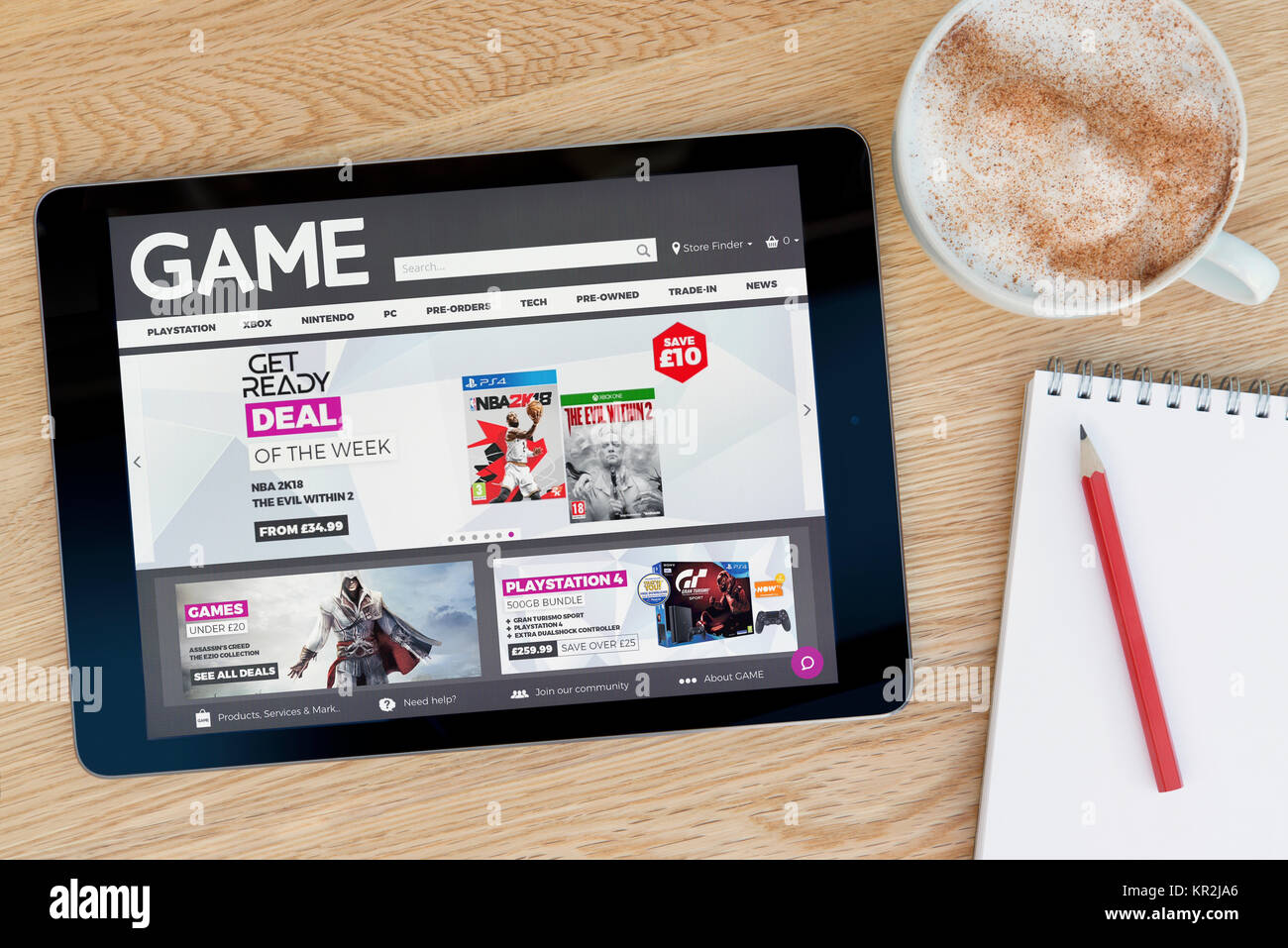 The Game retailer website on an iPad tablet device which rests on a wooden table beside a notepad and pencil and a cup of coffee (Editorial only) Stock Photo
