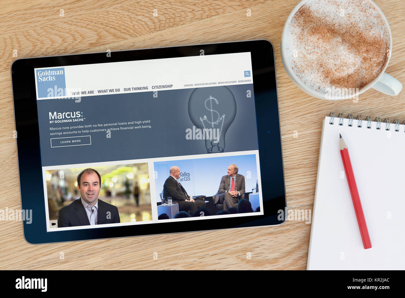 The Goldman Sachs website on an iPad tablet device which rests on a wooden table beside a notepad and pencil and a cup of coffee (Editorial only) Stock Photo