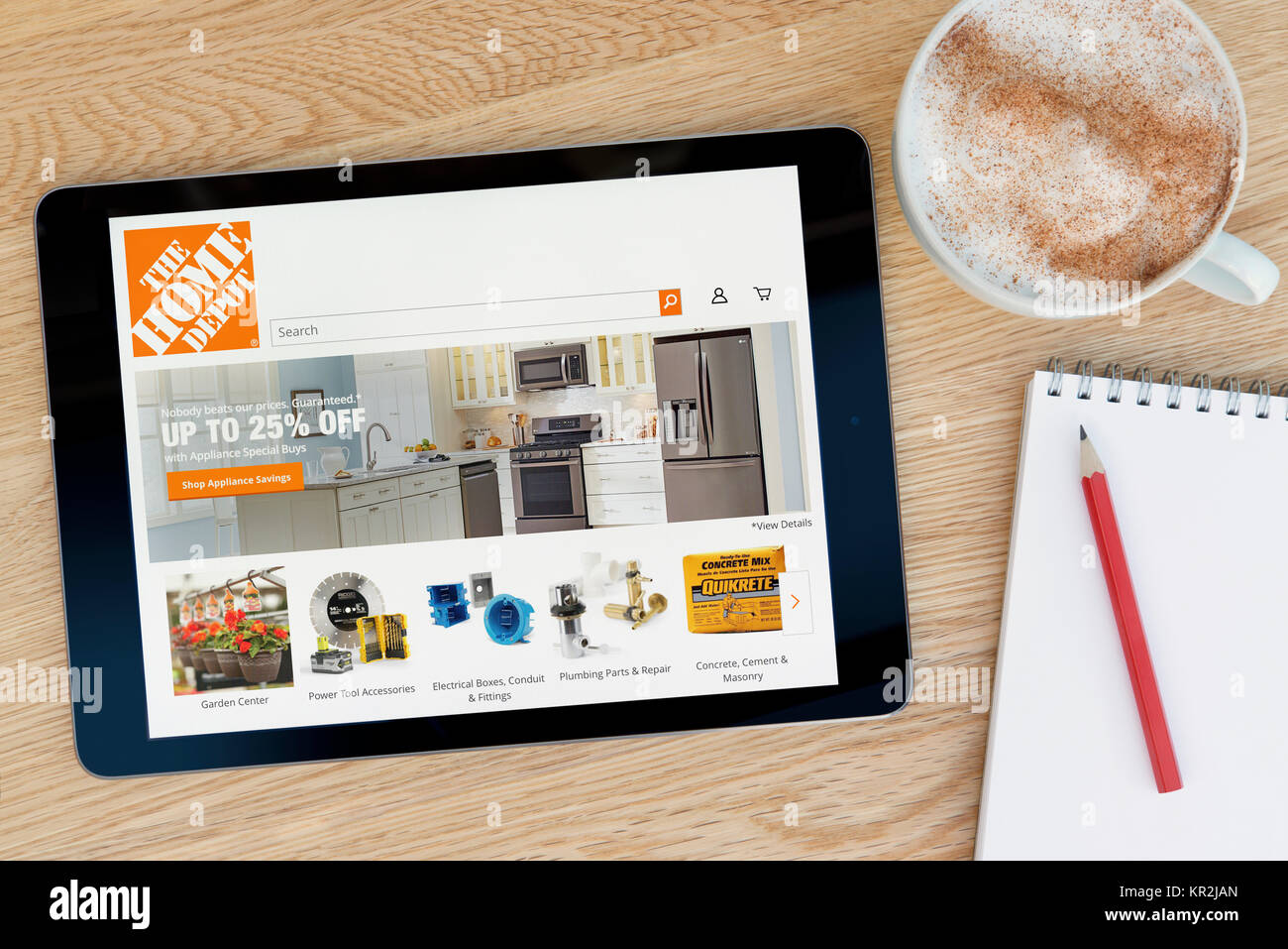The Home Depot website on an iPad tablet device which rests on a wooden table beside a notepad and pencil and a cup of coffee (Editorial only) Stock Photo