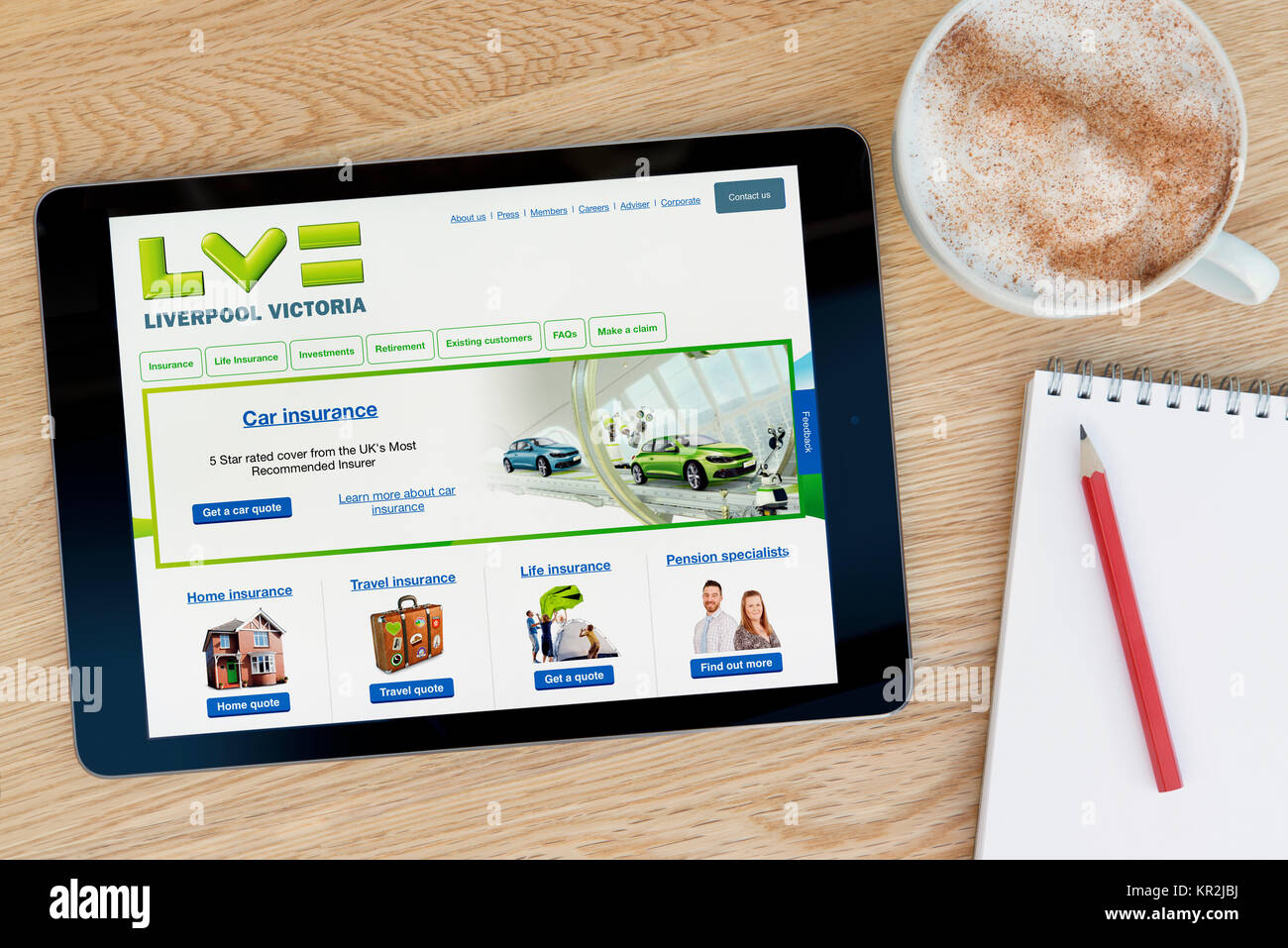 The Liverpool Victoria website on an iPad tablet device which rests on a wooden table beside a notepad and pencil and a cup of coffee (Editorial only) Stock Photo