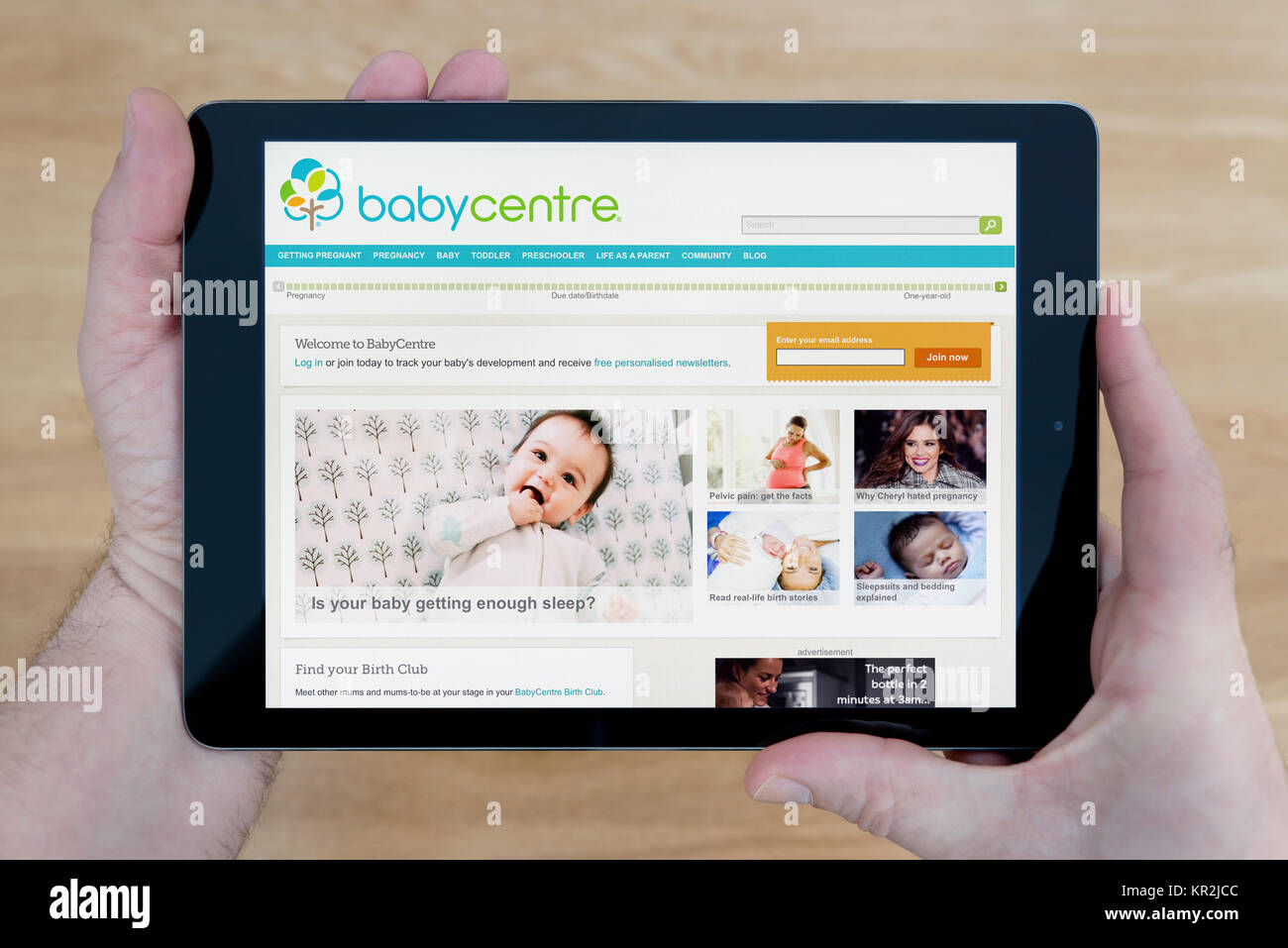 A man looks at the Baby Centre website on his iPad tablet device, shot against a wooden table top background (Editorial use only) Stock Photo