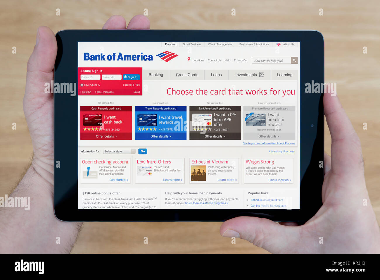 A man looks at the Bank of America website on his iPad tablet device, shot against a wooden table top background (Editorial use only) Stock Photo