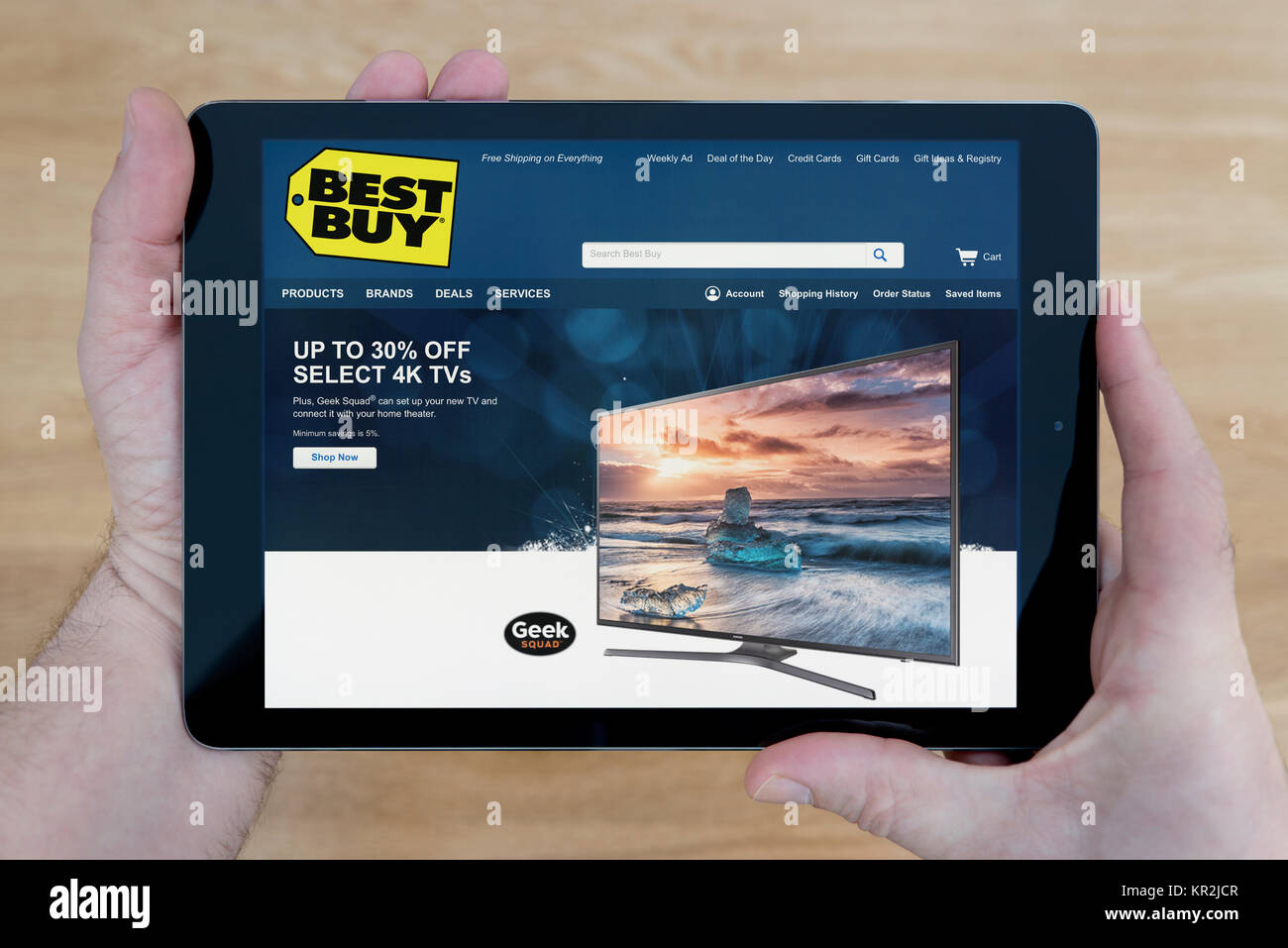 A man looks at the Best Buy website on his iPad tablet device, shot against a wooden table top background (Editorial use only) Stock Photo
