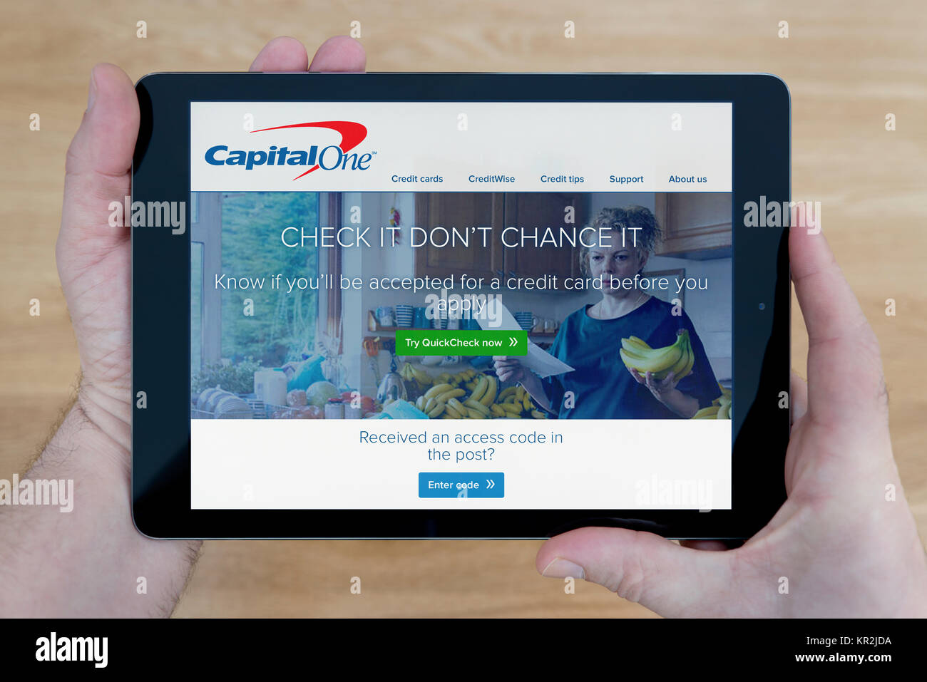 A man looks at the Capital One bank website on his iPad tablet device, shot against a wooden table top background (Editorial use only) Stock Photo