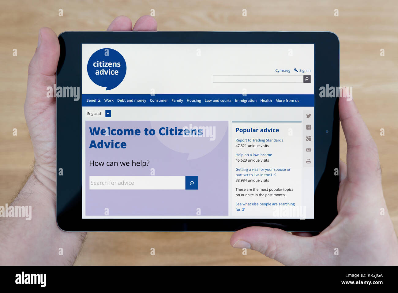 A man looks at the Citizens Advice website on his iPad tablet device, shot against a wooden table top background (Editorial use only) Stock Photo