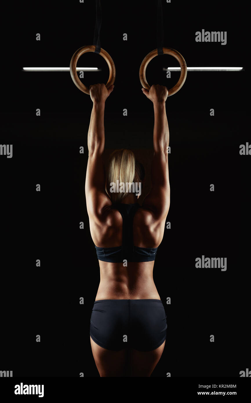 Veetical rearview shot of an athletic woman working out at the gym using gymnastic rings back