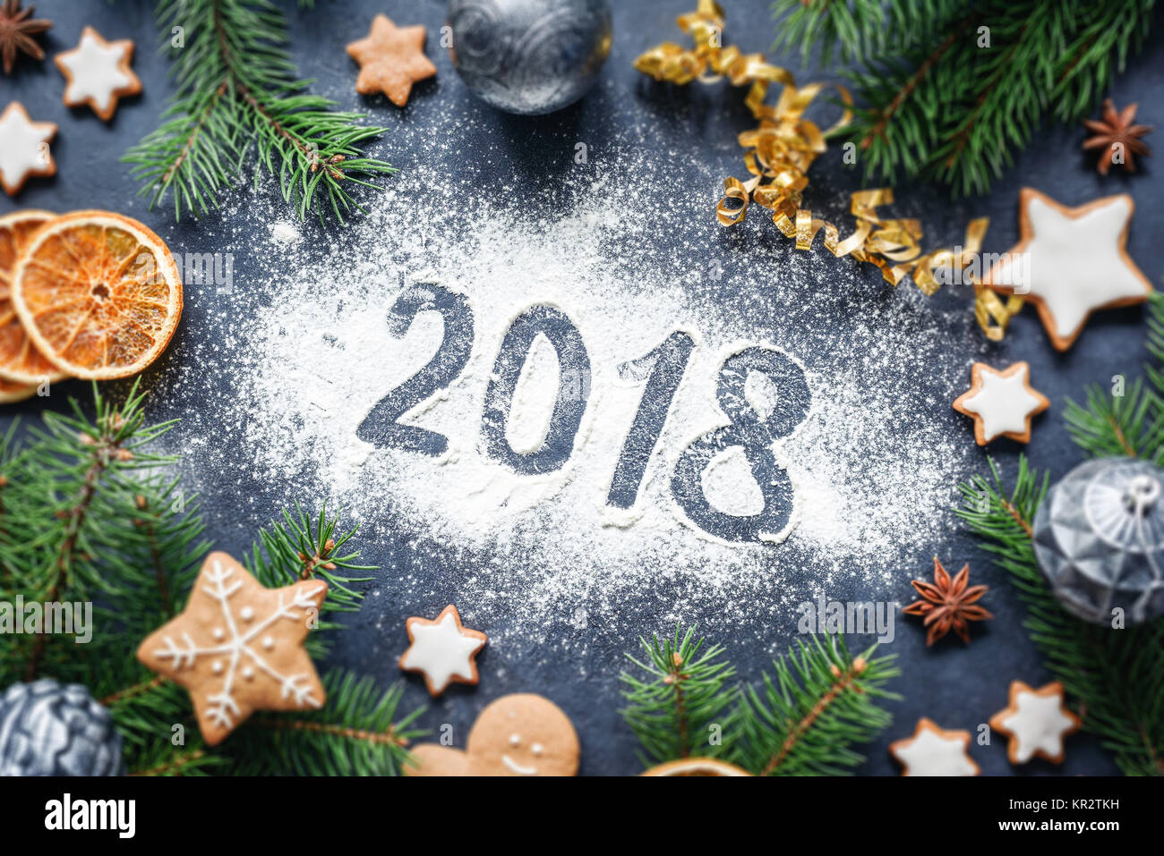 Happy New Year 2018 written on flour and Christmas Decorations Gingerbread cookies, cinnamon, oranges, spices, nuts and toys on concrete background. C Stock Photo