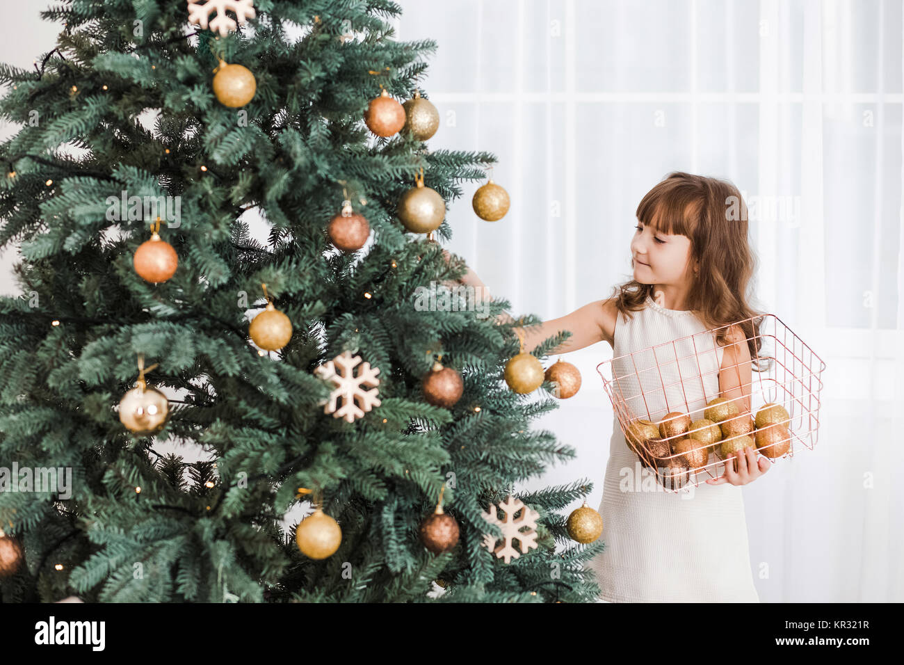 Beautiful little girl decorates huge green Christmas tree for holiday