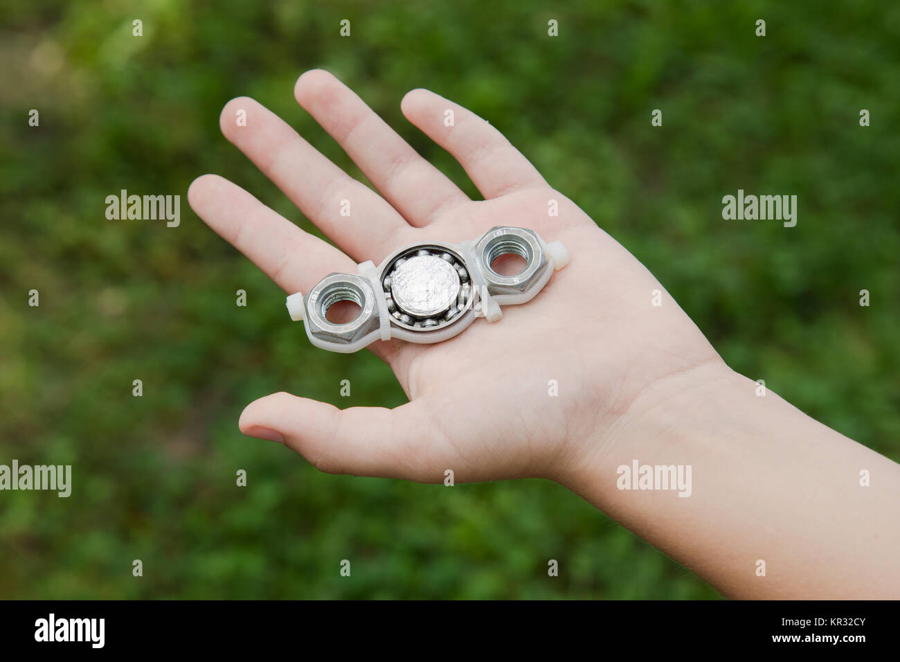 Closeup of hand of white kid playing modern popular hand toy spinner made by himself by using screw-nuts and bearing. Child holding unusual metal spin Stock Photo