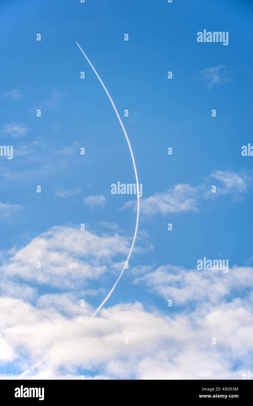 Curved contrail. Jet airliner plane flying at altitude leaving curving contrails vapour trail at height in the blue sky. Vapor trail Stock Photo