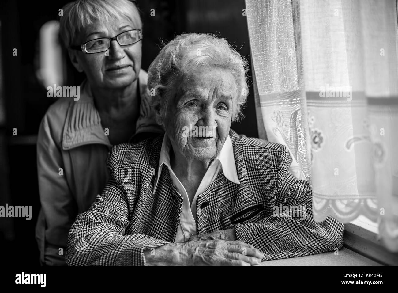 An elderly woman sitting at the table, next to a grown daughter. Black and white photo. Stock Photo