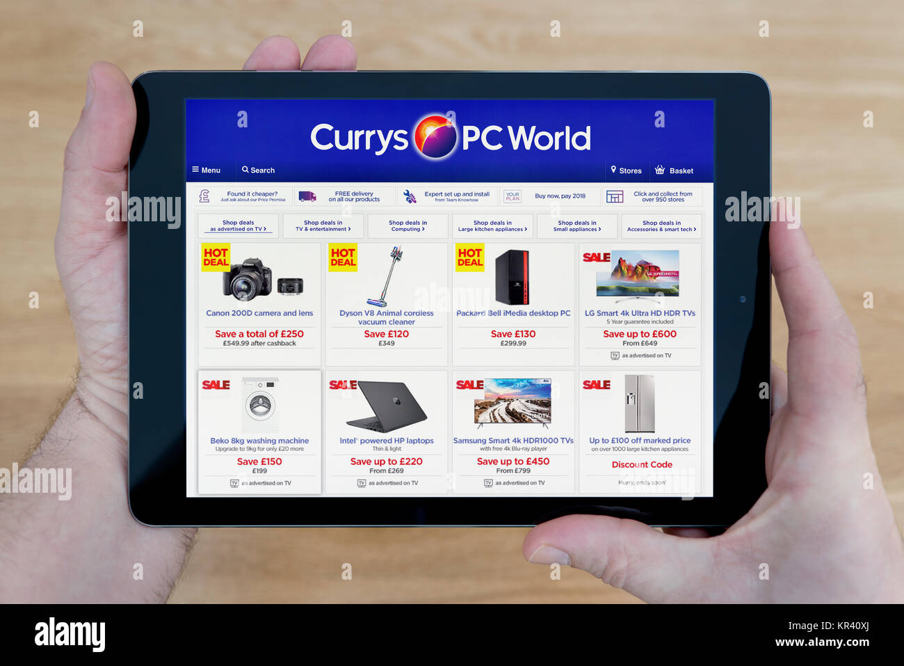 A man looks at the Currys PC World website on his iPad tablet device, shot against a wooden table top background (Editorial use only) Stock Photo