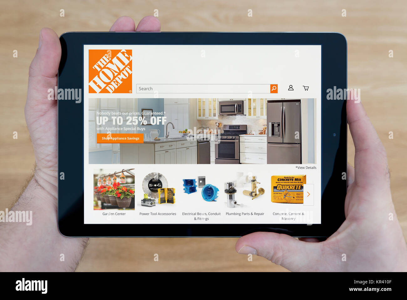 A man looks at the Home Depot website on his iPad tablet device, shot against a wooden table top background (Editorial use only) Stock Photo