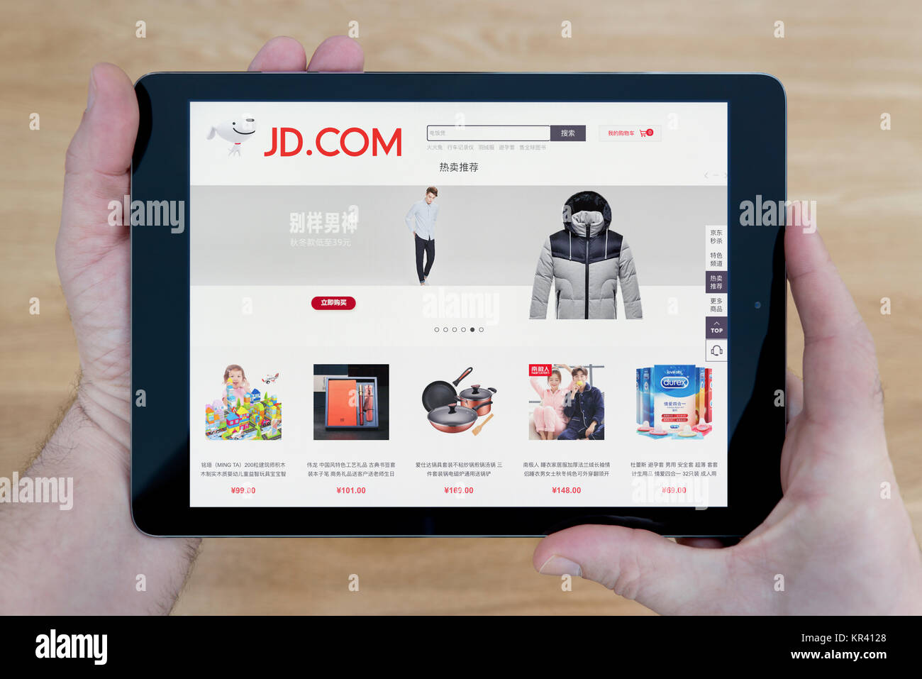 A man looks at the JD.com website on his iPad tablet device, shot against a wooden table top background (Editorial use only) Stock Photo