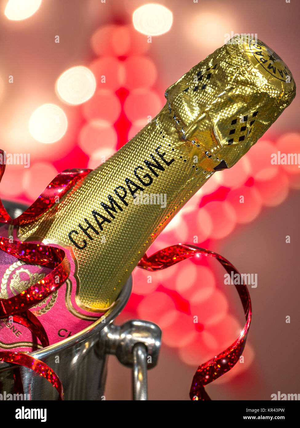 CHAMPAGNE PARTY LIGHTS Champagne bottle on ice in wine cooler champagne ice bucket, with Christmas party streamer and sparkling celebration lights Stock Photo