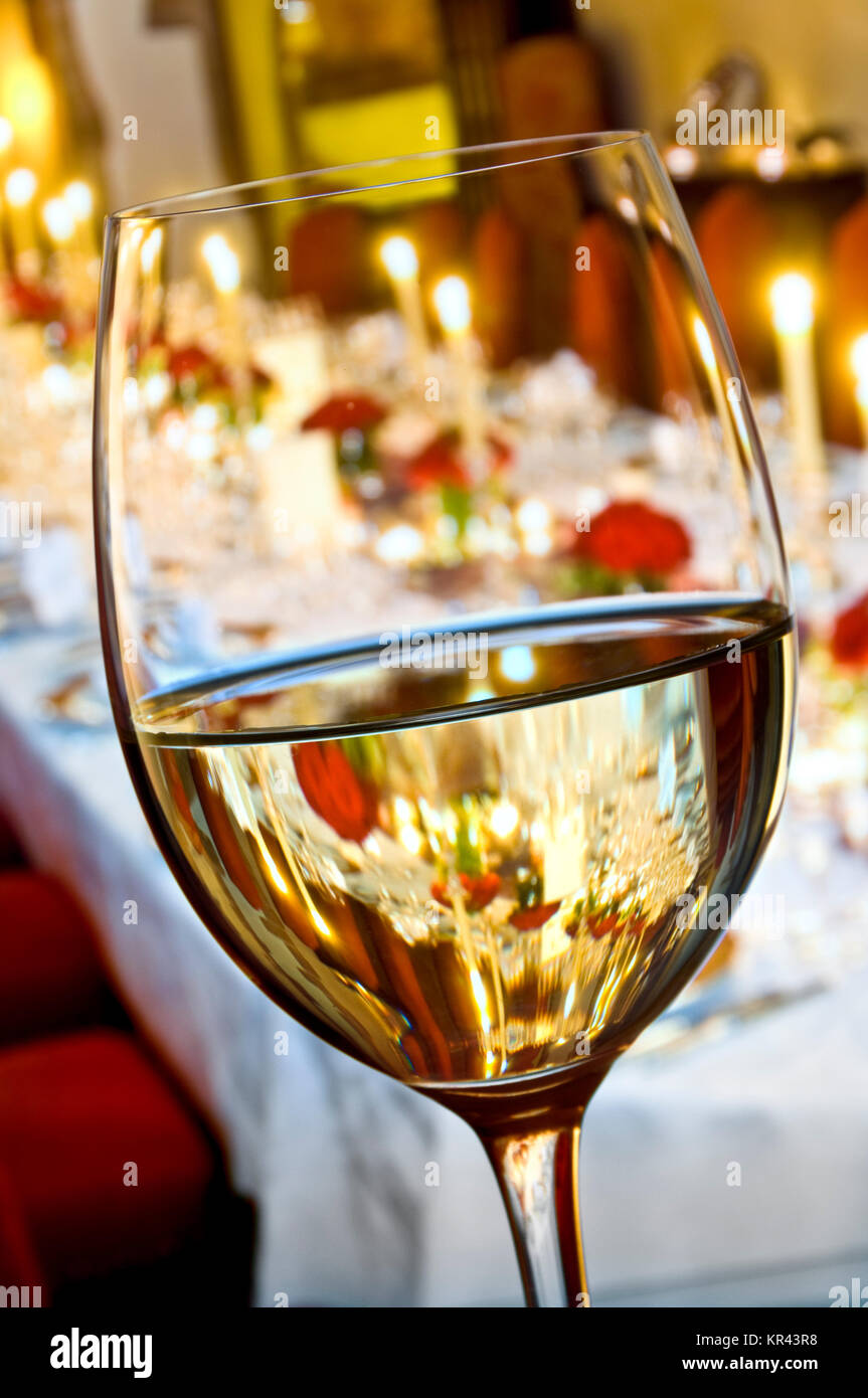 WINE DINNER TABLE CANDLES FORMAL TASTING Fine white wine glass in foreground of a formal seated candlelit dinner party table behind Stock Photo