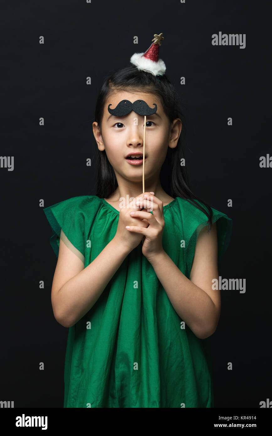 Cute asian woman child with fake mustache and christmas head decoration on black background Stock Photo