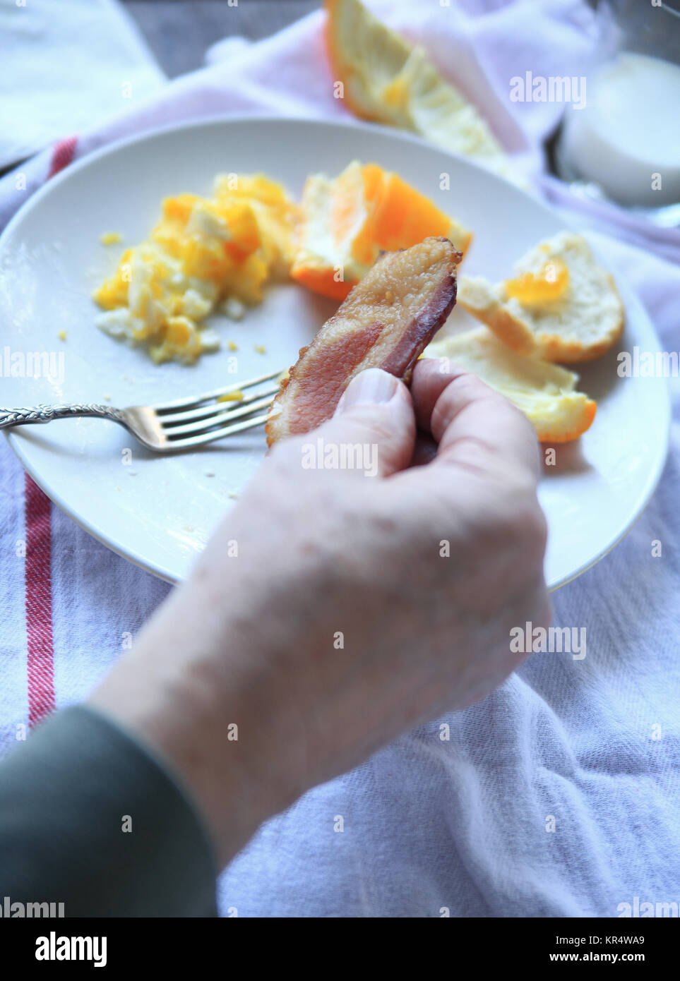 Man holds slice of bacon at breakfast Stock Photo