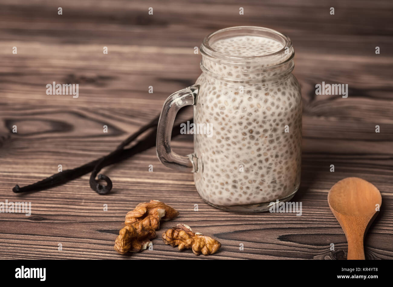 chia seed pudding in glass cup, walnuts, vanilla pods and spoon on wooden background, vegetarian food concept Stock Photo