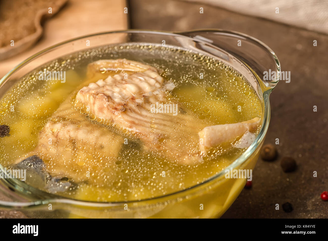 fresh fish soup with sturgeon, potatoes in transparent plate, decorated spices and rye bread on stone background, healthy eating, close up Stock Photo