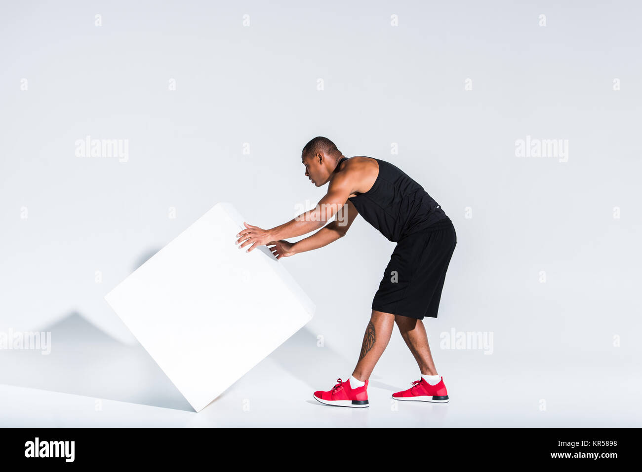 young african american sportsman moving white cube on grey Stock Photo
