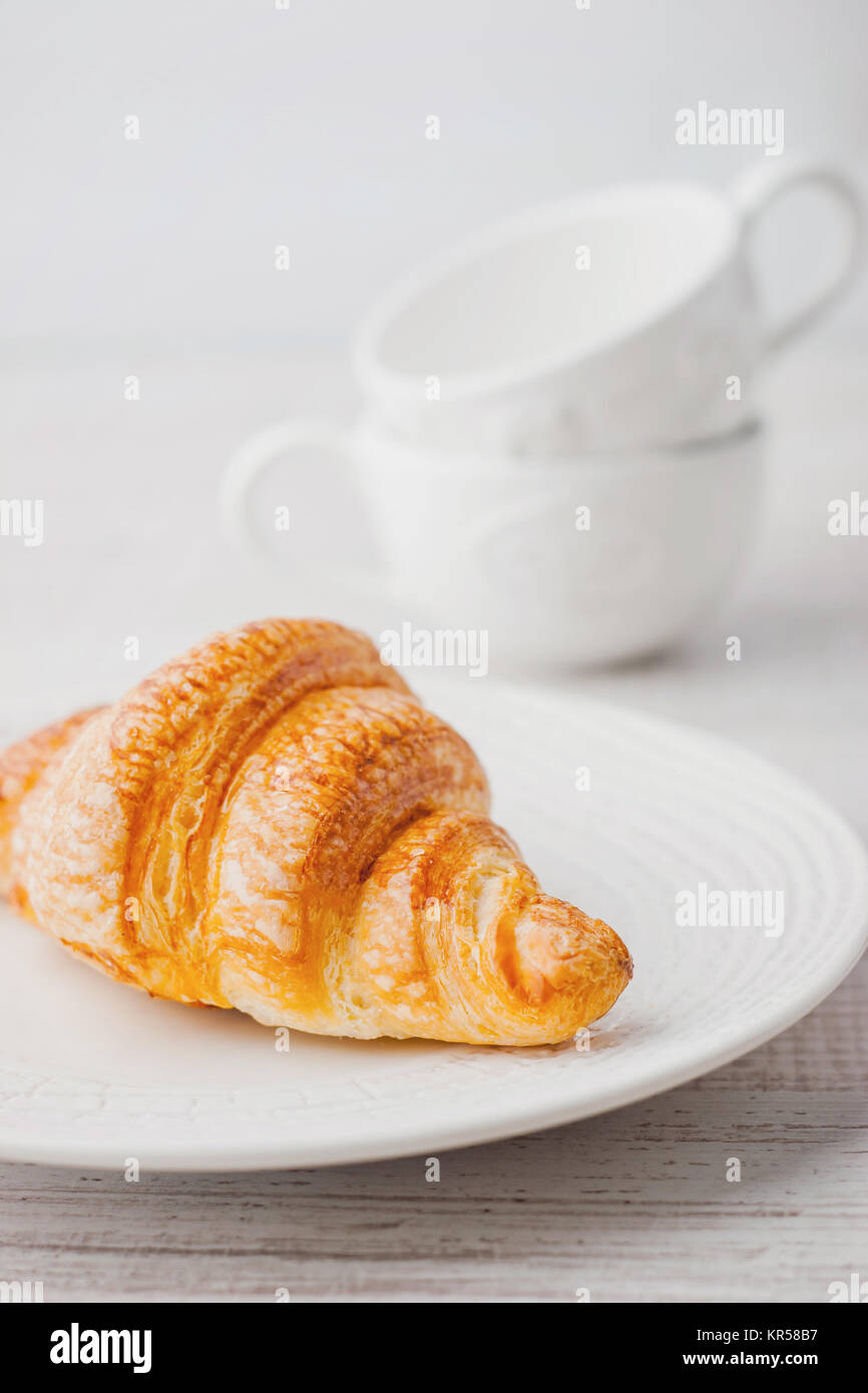 Croissant on the white plate with two blurred cups vertical Stock Photo