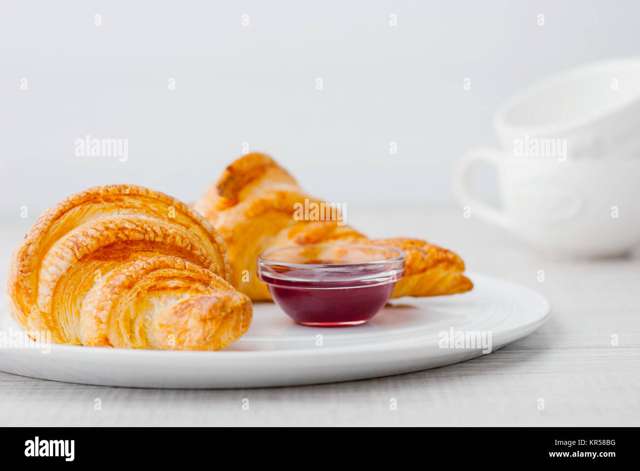 Croissants with berry jam and two white blurred cups horizontal Stock Photo