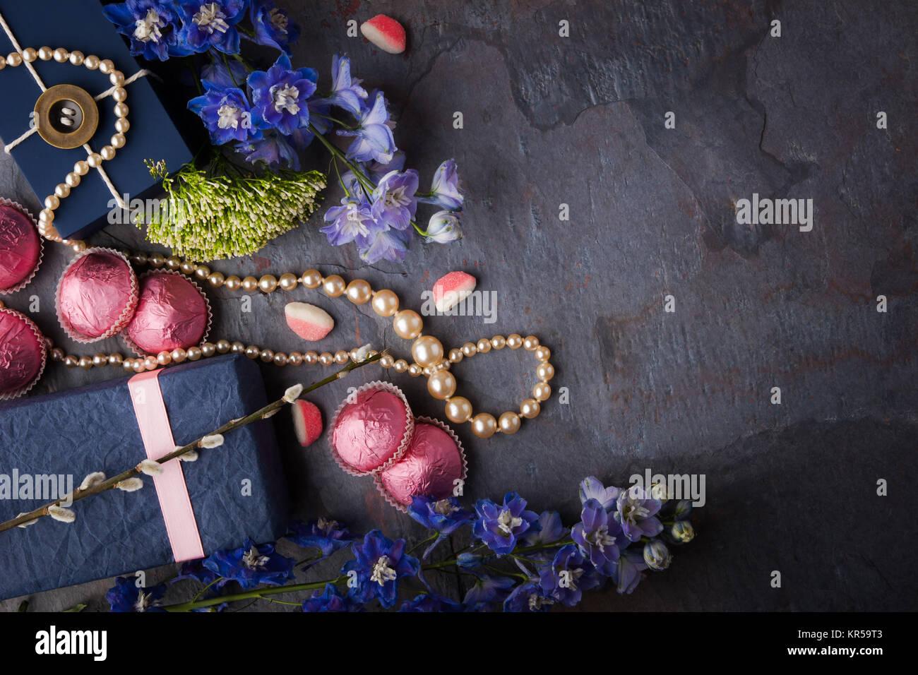 Spring gift with candy, pearl necklace and flowers on a blue stone background Stock Photo