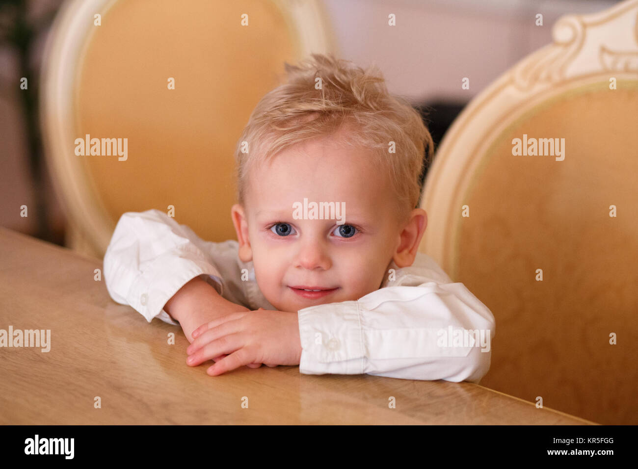 Cute Blonde Hair Little Boy Is Sitting At The Table Stock