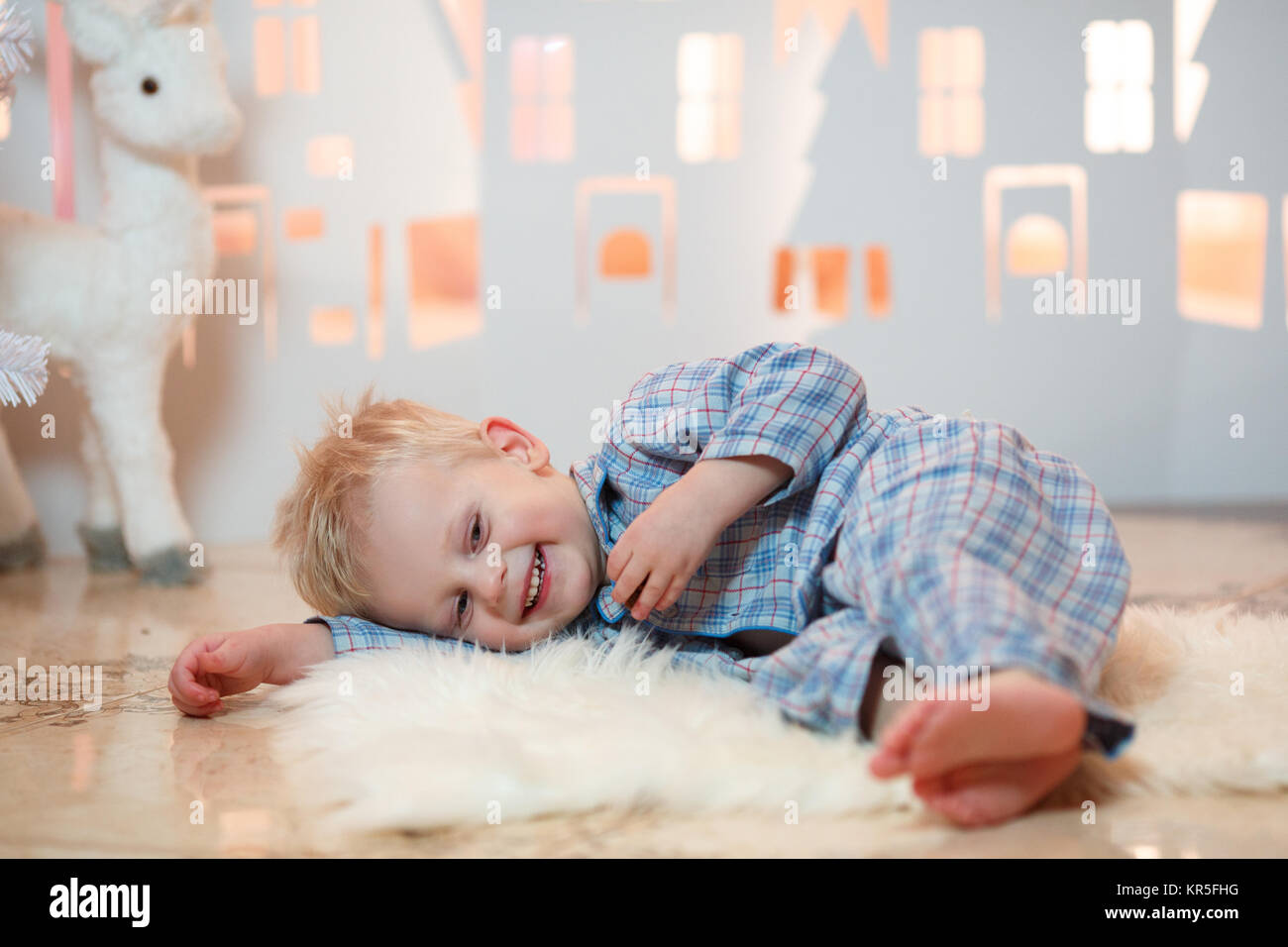 Cute blonde hair little boy in sleepwear near christmas toy paper houses. Stock Photo