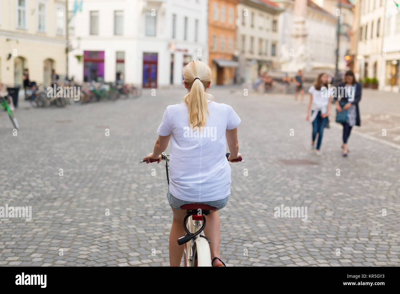 Beautiful blond caucasian woman riding bike in the city center Stock