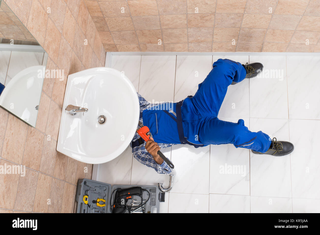 Plumber Lying On Floor Repairing Sink In Bathroom Stock Photo