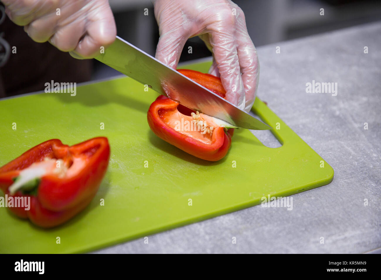 Salad preparation - hands in gloves cutting red pepper into pieces Stock Photo