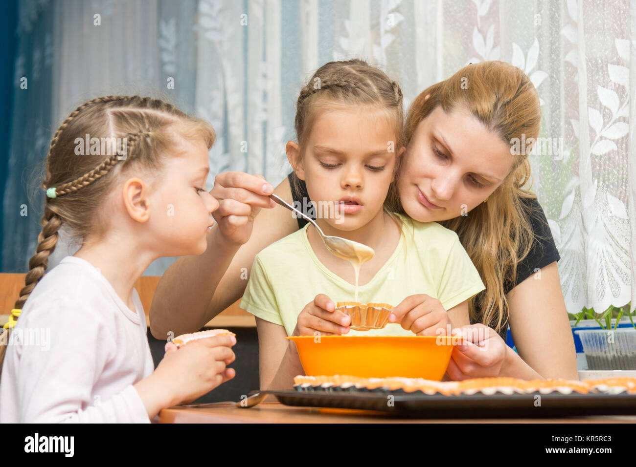Mother and two children baking pour the mass into molds preparing muffins for Easter Stock Photo