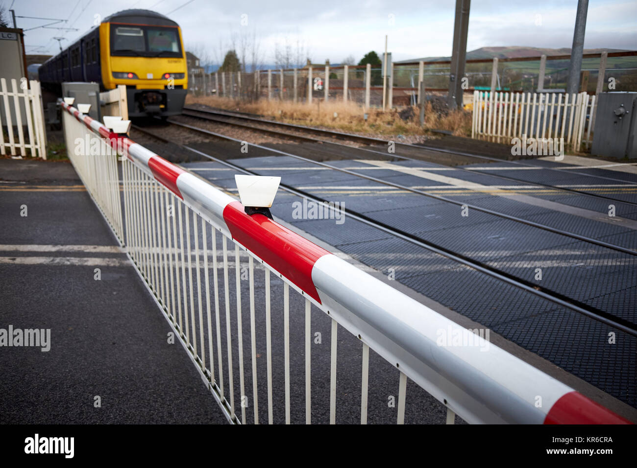 A train approaches an unmanned level crossing with the barriers / gates shut Stock Photo