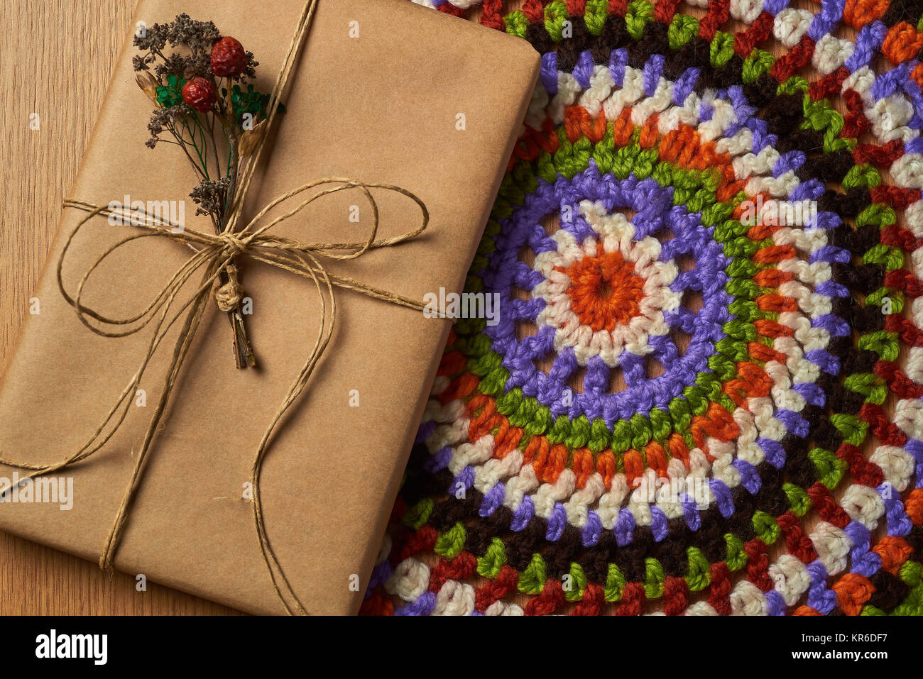 Wrapped book tied with brown paper thread with small dried bouquet of field plants is lying on the table on colorful knitted napkin. Stock Photo