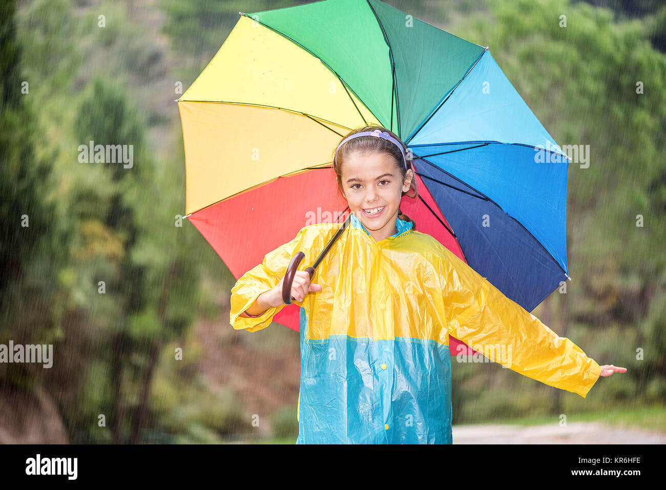 Happy little girl with colorful umbrella and raincoat playing in the
