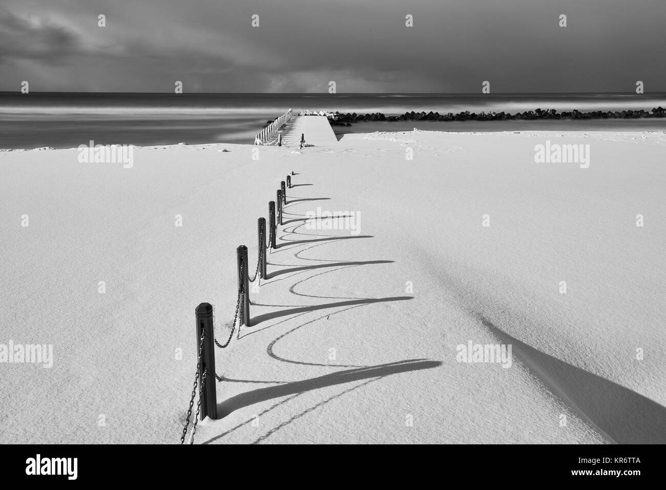 Fence running along a snow-covered beach near the ocean in winter. Stock Photo