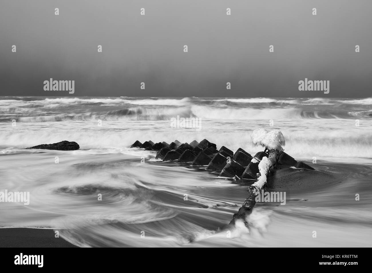 Snow-covered wave breakers on a rocky beach in winter. Stock Photo