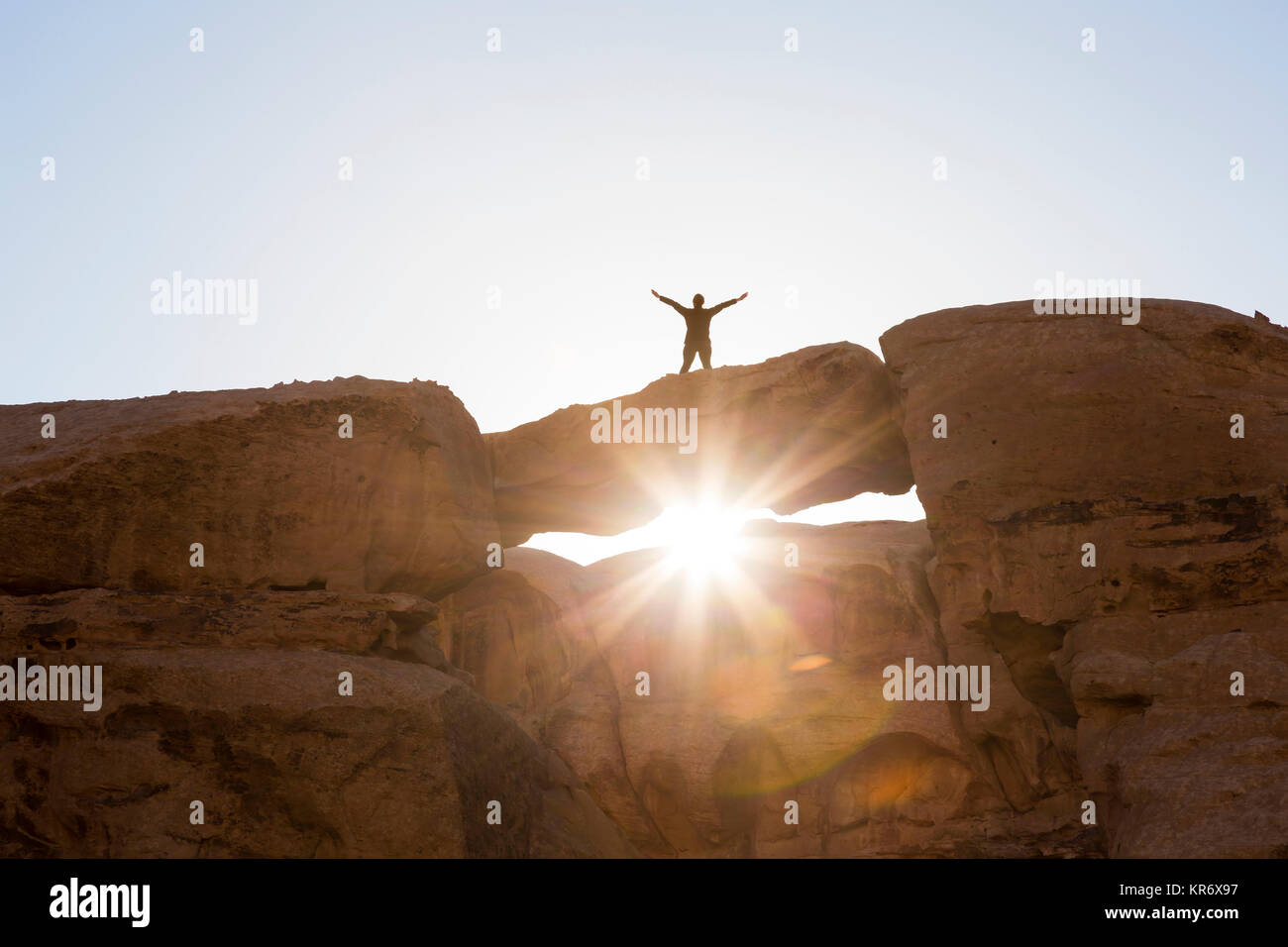Low angle view of woman standing with her arms outstretched on a natural rock bridge in the desert. Stock Photo