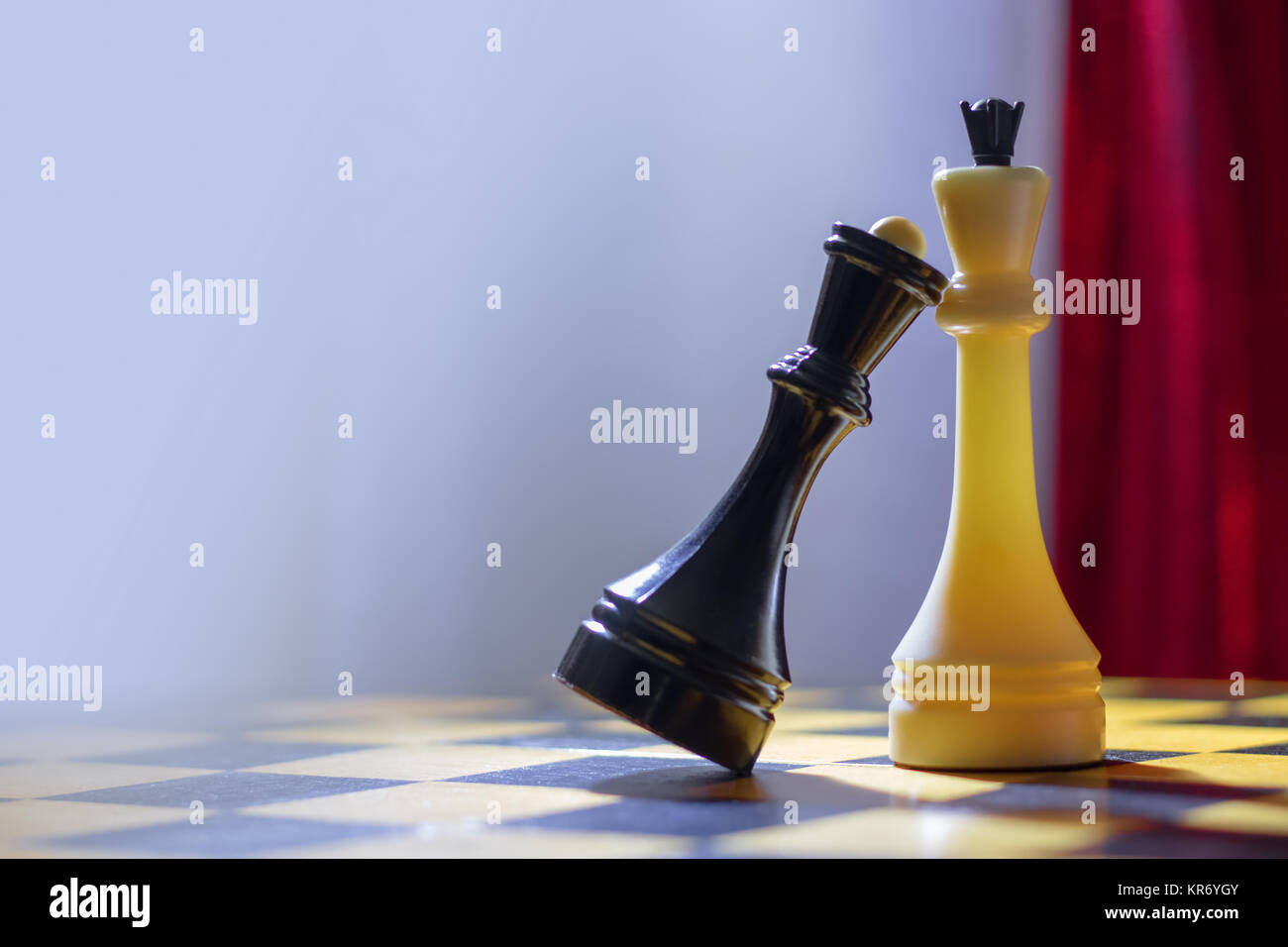 Chess black queen and white king stand on a wooden chessboard. The black queen put her head on the chest to the white king. Stock Photo