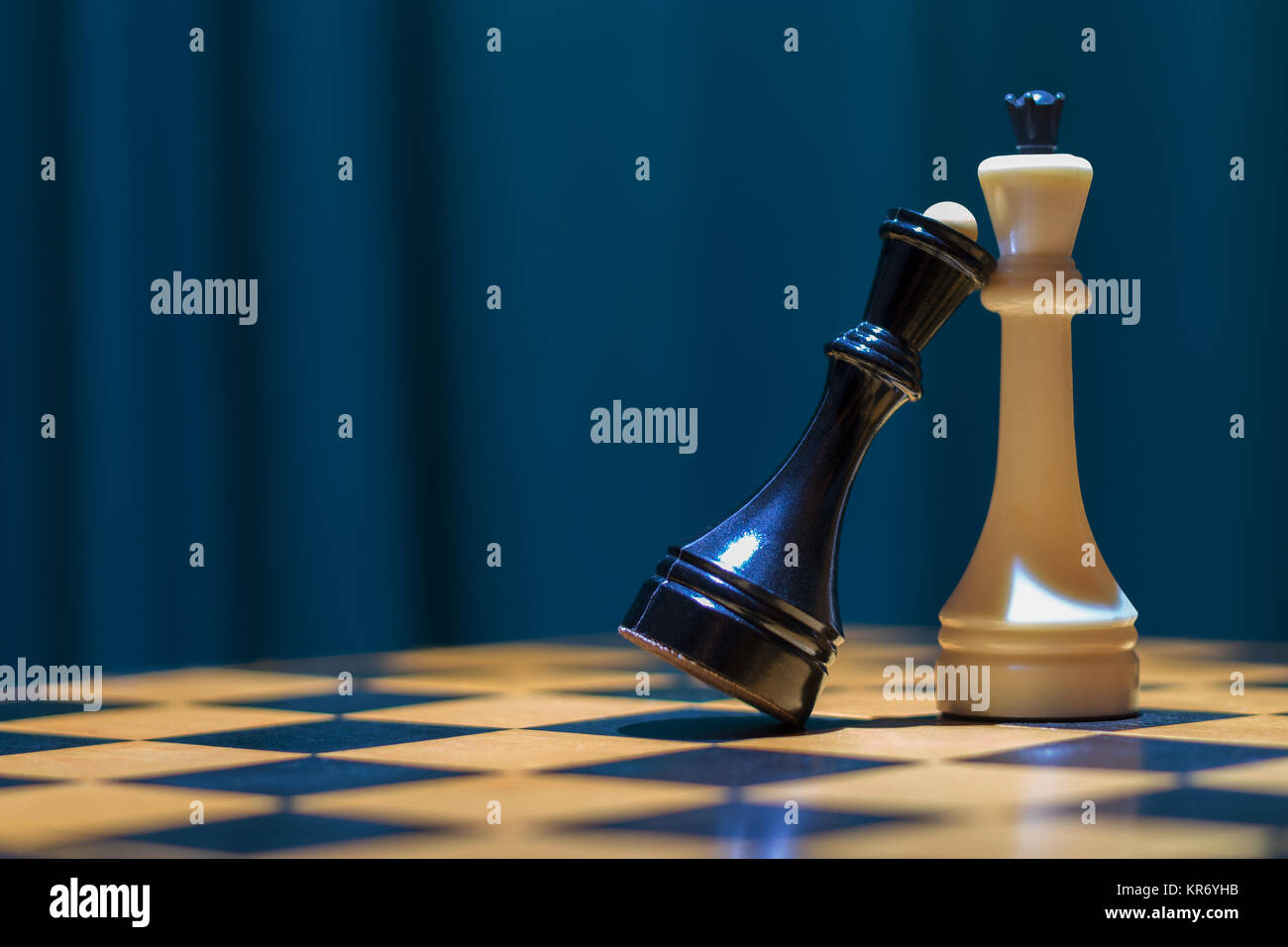 Chess black queen and white king stand on a wooden chessboard. The black queen put her head on the chest to the white king. Stock Photo