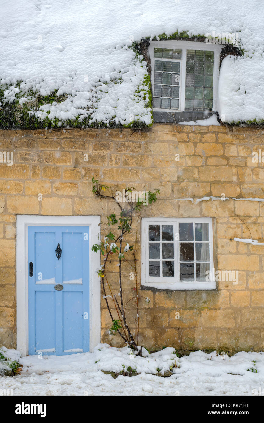 Snow covered thatched cottage with a light blue front door in Broadway