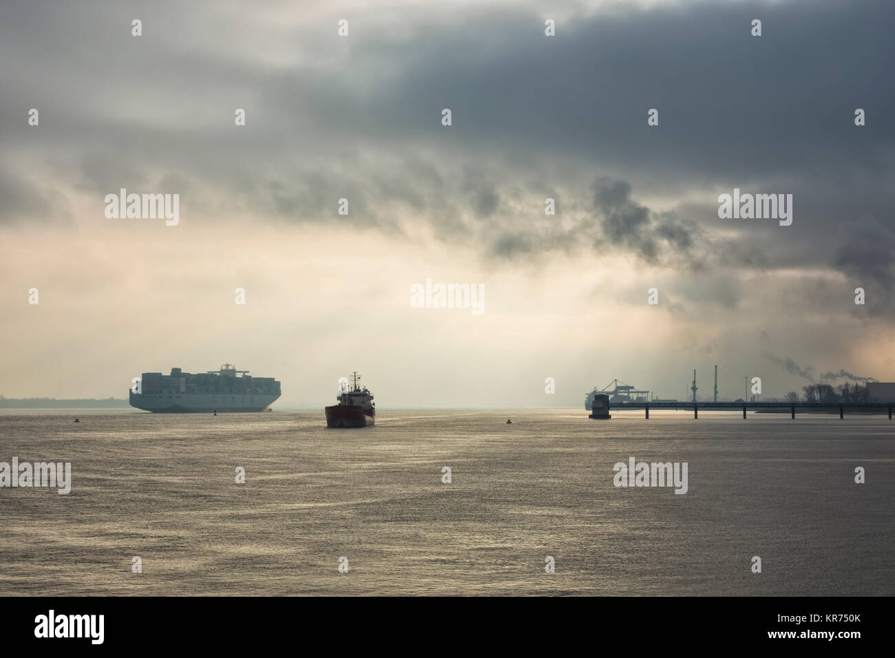 Container ship COSCO DENMARK on Elbe river heading towards Hamburg on a misty morning, passing a moored tanker Stock Photo