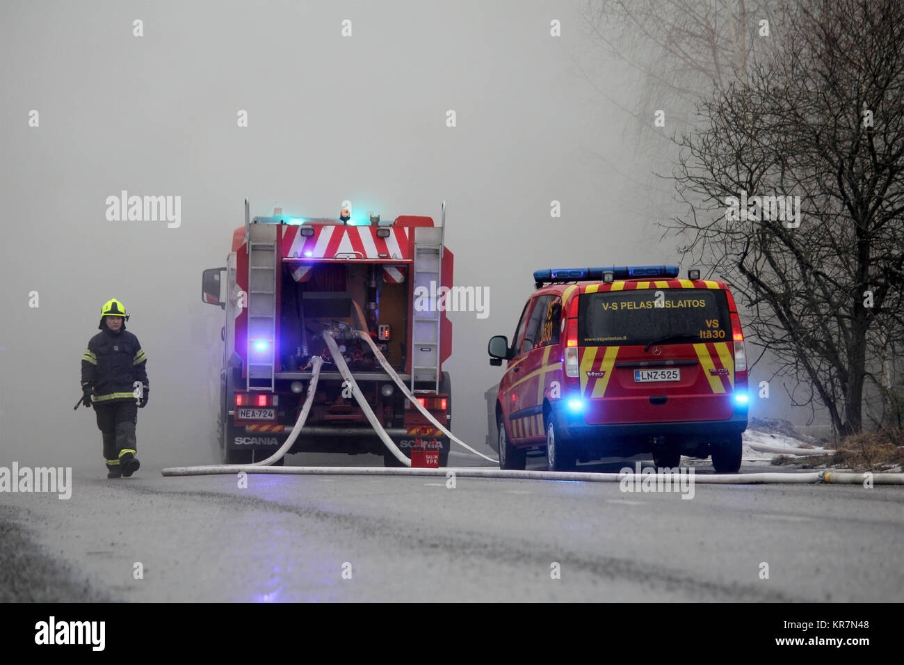 SALO, FINLAND - FEBRUARY 16, 2014: Firefighter emerges from heavy smoke at the fire scene of Salo Cement Plant, with two fire trucks on the street. Stock Photo