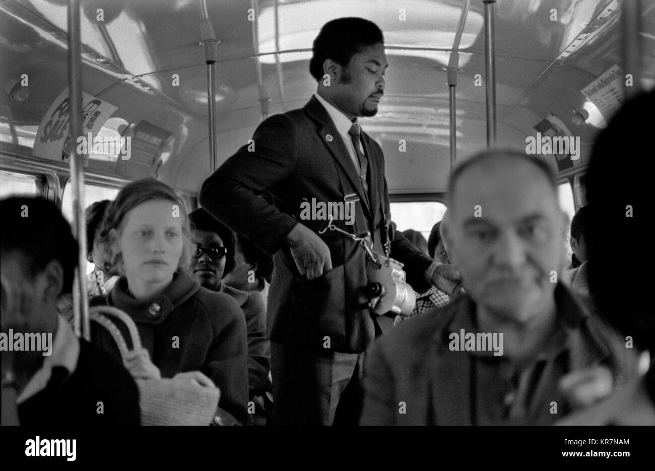 Bus conductor walking up and down the bus, this is the upper deck of a double decker bus. He is taking peoples fare money and giving them  tickets from his ticket machine, thats slung around his neck and shoulders and seen on his chest. 1970s London multi ethnic Britain 70s HOMER SYKES Stock Photo