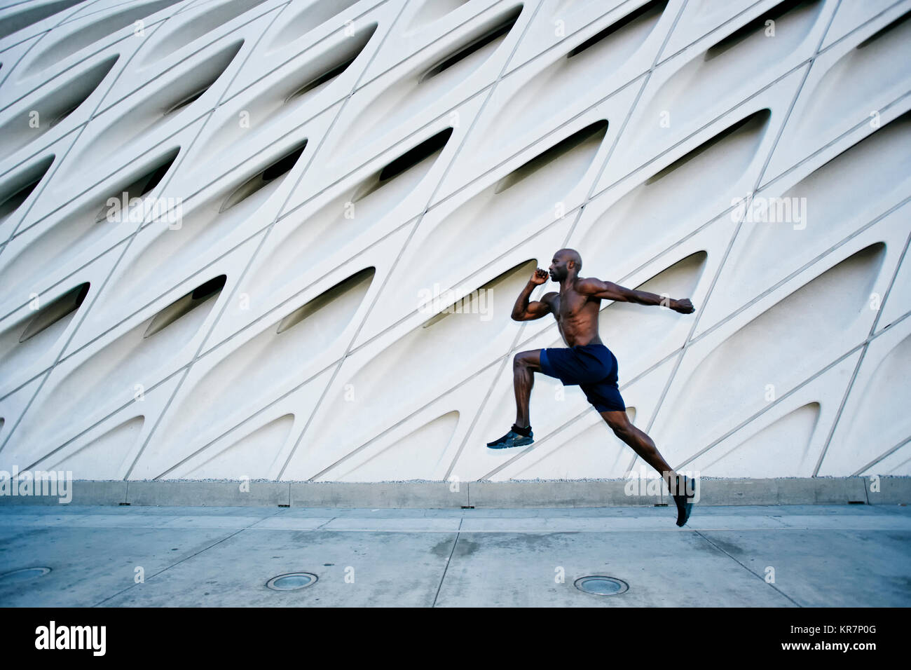 Black man running and jumping on sidewalk Stock Photo