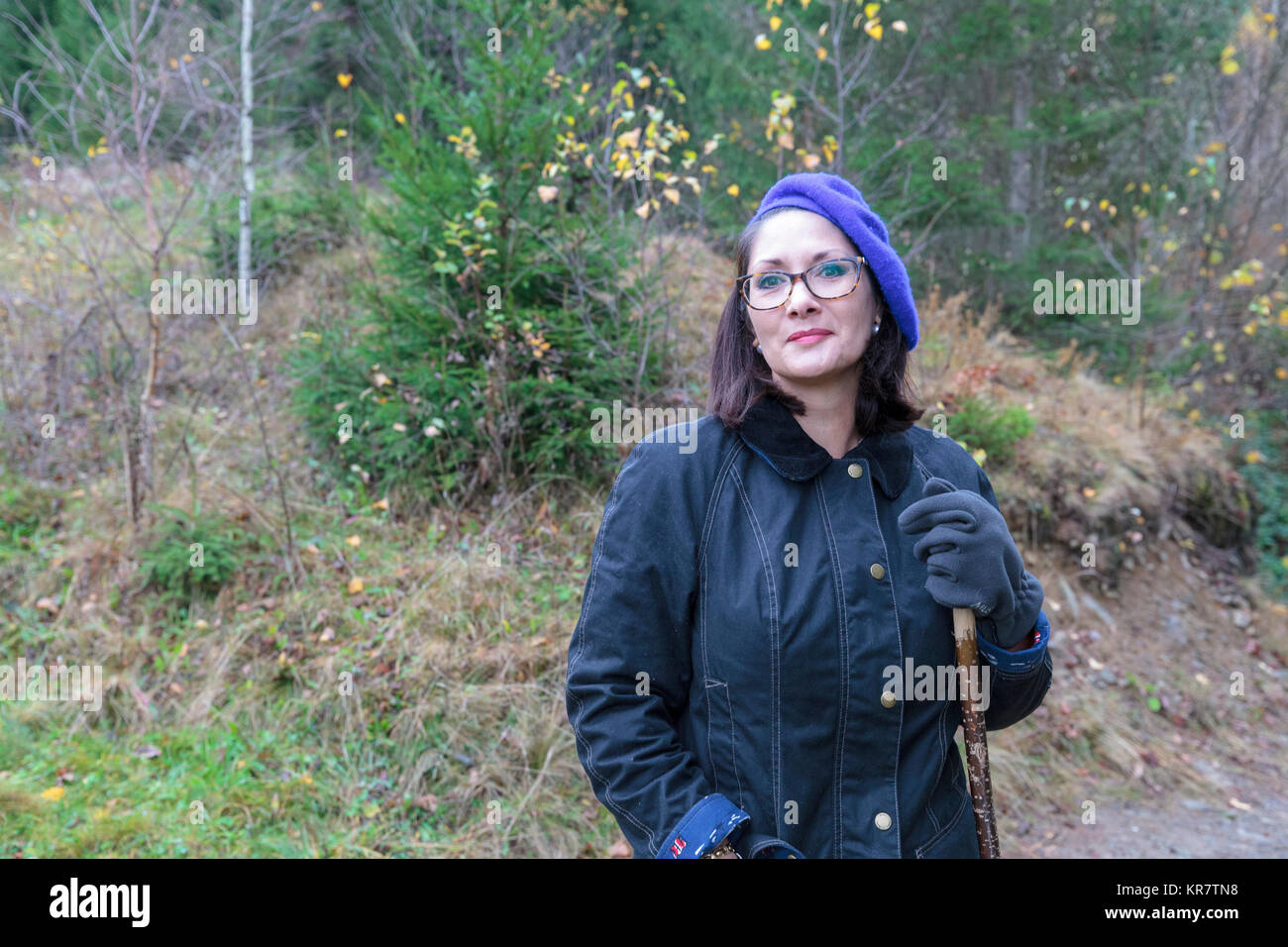Lady with glasses wearing blue beret standing in the woods Stock Photo